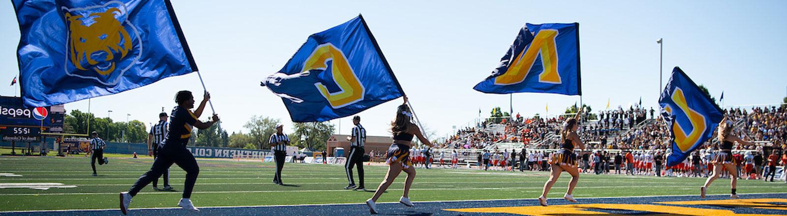 Cheerleaders running with flags that spell UNC in the endzone of the football field.