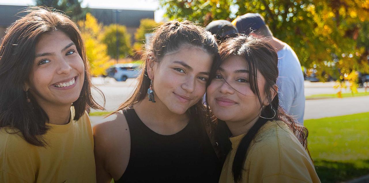 Three college students smiling and standing together outside during an event to celebrate Hispanic/Latinx communities